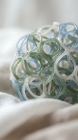 Colorful silicone rubber bands in blue and green tones arranged in artistic pile on soft fabric background for craft and office supplies concept.