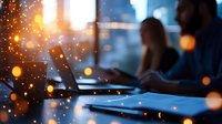 Young diverse business team working late at office with laptops and digital devices, blurred silhouettes against window with bokeh light effects.