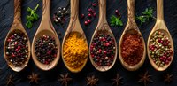 Aromatic spices and peppercorns in wooden spoons on dark background, overhead view of colorful turmeric, paprika and mixed peppercorns for cooking.