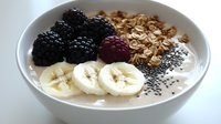 Healthy breakfast bowl with yogurt, fresh blackberries, sliced banana, granola, and chia seeds on white ceramic bowl. Clean eating and nutritious morning meal.