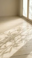 Empty room corner with natural light casting tree branch shadows on wooden floor through large windows creating peaceful interior atmosphere.