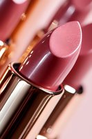 Close-up macro shot of pink glossy lipstick in metallic holder against blurred background, showcasing luxury cosmetic product detail and texture.
