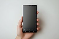 Hand holding modern black smartphone with blank screen against neutral background, minimalist composition for mobile app and technology mockup designs.