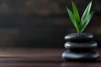 Stacked black spa stones with fresh bamboo leaves on dark wooden surface against moody background, wellness and zen concept for spa treatments.