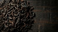 Dried tea leaves scattered on dark wooden surface, overhead view with copy space for beverage, culinary, or wellness design projects.