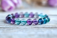 Colorful fluorite crystal bracelet with alternating purple, blue and turquoise beads on rustic white wooden background, showcasing natural gemstone jewelry.