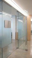Modern office interior with glass partition walls and wooden accents creating transparent workspace divisions in contemporary corporate environment.