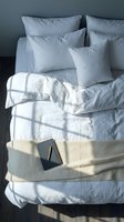 Cozy bed with white linen bedding, soft pillows, a notebook and pen in warm morning sunlight, top view, minimal bedroom interior.