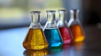 Colorful laboratory flasks containing yellow, blue, red and orange liquids arranged in row on reflective surface with soft focus background for science concept.