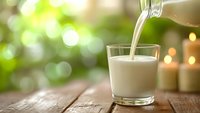 Fresh milk being poured into glass on wooden table with natural bokeh background for healthy breakfast and dairy nutrition concepts.