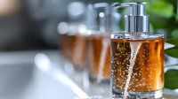 Elegant glass soap dispenser with amber liquid and chrome pump on blurred bathroom counter, soft focus creates luxurious spa atmosphere with natural light.