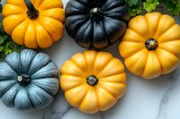 Fresh orange and black decorative pumpkins on marble background with green leaves. Seasonal autumn harvest composition for Halloween and fall decor.