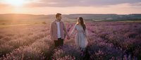 Couple holding hands in blooming lavender field at golden hour sunset, romantic engagement or wedding portrait session in rural countryside landscape.