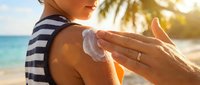Young woman applying sunscreen lotion on shoulder at tropical beach during summer vacation, sun protection skincare routine.