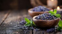 Dried lavender flowers in wooden bowls with fresh mint leaves on rustic wood table. Natural aromatherapy herbs for spa treatments and relaxation.
