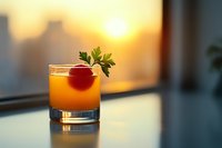 Orange cocktail garnished with fresh parsley and cherry in rocks glass against blurred sunset cityscape background, creating warm atmospheric mood for beverage photography.