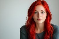 Young woman with vibrant red hair and green eyes wearing dark sweater poses against light background, natural makeup and soft smile for beauty portrait.