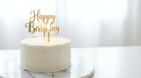 White birthday cake with golden Happy Birthday topper on marble stand, elegant minimalist celebration dessert for party decoration.
