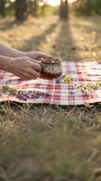 Senior woman hands holding ceramic mug on checkered blanket during outdoor picnic with lavender flowers in warm golden hour sunlight for relaxation concept.