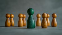 Green wooden figure stands out among brown pawns on gray background, representing leadership, uniqueness and individuality in business concept.
