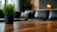 Green ornamental grass plant in black pot on wooden table surface with blurred modern interior background, creating minimalist home decor atmosphere.