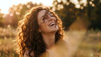 Young woman with curly hair laughing joyfully in golden sunset light outdoors. Natural happiness and positive emotions in warm evening glow.
