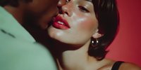 Intimate couple moment with woman in red lipstick and short dark hair against vibrant red background, romantic passion and desire concept for lifestyle content.