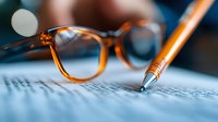 Brown tortoise shell reading glasses and pen on paper document with shallow depth of field, creating professional business composition for office and education concepts.