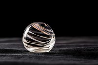 Clear glass sphere with elegant swirled patterns on dark textured surface for luxury product photography and modern interior design concepts.