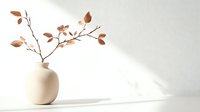 Minimalist autumn branch with copper leaves in round cream vase on white surface with soft shadow play.