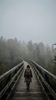 Hiker with backpack walking on wooden boardwalk bridge through misty forest landscape, adventure travel and outdoor exploration concept for nature tourism and hiking destinations.