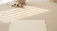 Blank white paper sheet on neutral beige surface with natural sunlight casting striped shadows, minimalist workspace setup for design mockups and branding presentations.