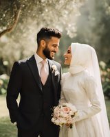 Happy Muslim newlywed couple in wedding attire sharing intimate moment outdoors with bride in hijab and groom in black suit holding bouquet.