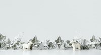 Frosted winter foliage arrangement with white reindeer figurines and candles on neutral background, suitable for holiday decorating and seasonal marketing materials.