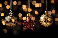 Elegant Christmas ornaments hanging against blurred golden bokeh lights, featuring gold baubles and a red star decoration.