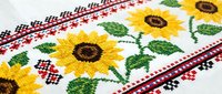 Vibrant cross-stitch embroidery with sunflowers and traditional folk ornaments on white linen fabric, showcasing handmade textile art.