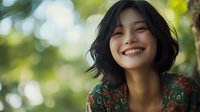 Young Asian woman with short black hair smiling genuinely outdoors, wearing floral pattern dress against natural bokeh background. Authentic happiness and joy concept.