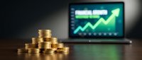Stacked gold coins with upward trending graph on laptop screen displaying financial growth and investment success metrics.