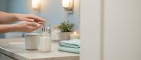 Woman dispensing liquid soap from pump bottle in modern bathroom with soft lighting and clean minimalist design for hygiene and wellness concepts.
