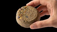 Hand holding a natural herbal solid shampoo bar with dried flowers, isolated on transparent background, ready for eco beauty, sticker, and print on demand design use.