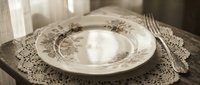 Elegant vintage porcelain plate with ornate botanical design on lace doily, styled for fine dining, table setting, and home decor projects.