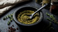 Ground green herbs and spices in stone mortar with pestle on dark slate surface. Cooking ingredients for seasoning and flavoring dishes.