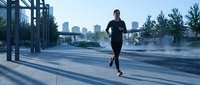 Athletic male runner jogging on urban waterfront promenade at sunrise with city skyline in background, fitness and outdoor exercise concept.