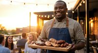 Happy African American chef presenting grilled meat platter at outdoor restaurant during golden hour sunset with string lights creating warm ambiance.