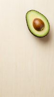 Fresh halved avocado with pit on light wooden surface, suitable for food, nutrition, healthy eating, and culinary content.