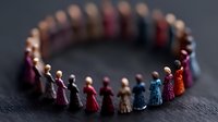Small colorful wooden figures holding hands in circle formation on dark textured background symbolizing unity, diversity, community and teamwork concept.
