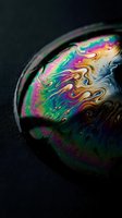 Iridescent soap bubble with swirling rainbow colors on dark background, macro shot capturing vivid holographic liquid surface texture.