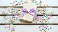 Handmade gift card with purple ribbon bow surrounded by colorful paper hearts on rustic wooden background for Valentine's Day celebrations.