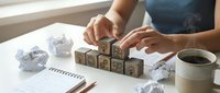 Woman arranging wooden letter blocks spelling FUTURE on desk with crumpled papers and coffee cup, planning and goal setting concept for business success.
