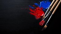 Paint brushes with vibrant red and blue acrylic paint strokes on dark wooden background, artistic composition showing texture and contrast of colors.